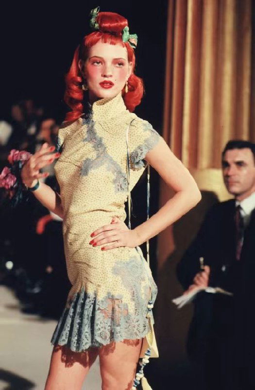 Модель в коротком платье с кружевными вставками и волнистой причёской на показе Dior 1998, акцент на женственных линиях и ретро‑деталях наряда.