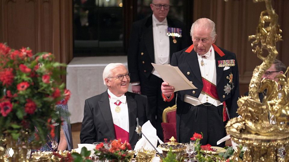 Крупный кадр короля у трибуны и общие планы за столом; залы украшены золотом, цветами и подсвечниками для официального банкета.