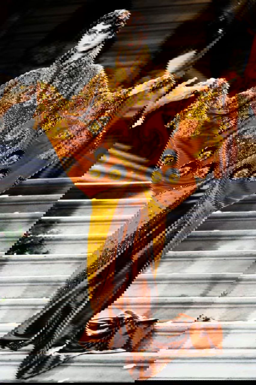 Модель в роскошном золотом плаще с богатой вышивкой и украшениями, спускается по мармурной лестнице — кадр из кутюрного показа Dior 1998 года.