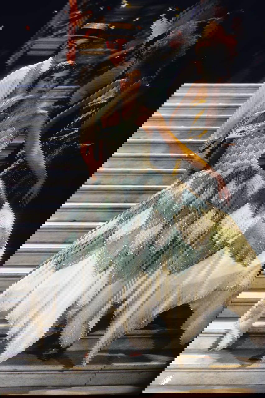 Балетный силуэт в многослойном бело-зелёном платье с лепестковыми деталями и блёстками, модель на лестнице в сценической постановке показа Dior 1998.