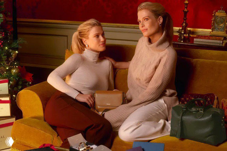 Близняшки Спенсер сидят на диване в роскошной интерьере праздничной сцены и демонстрируют авторские сумочки Aspinal в тёплом свете.