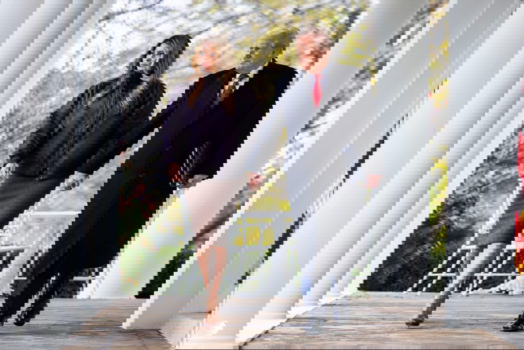 Широкий план: Мелания Трамп и Дональд Трамп идут по колоннаде Белого дома, осенняя листва на заднем фоне.