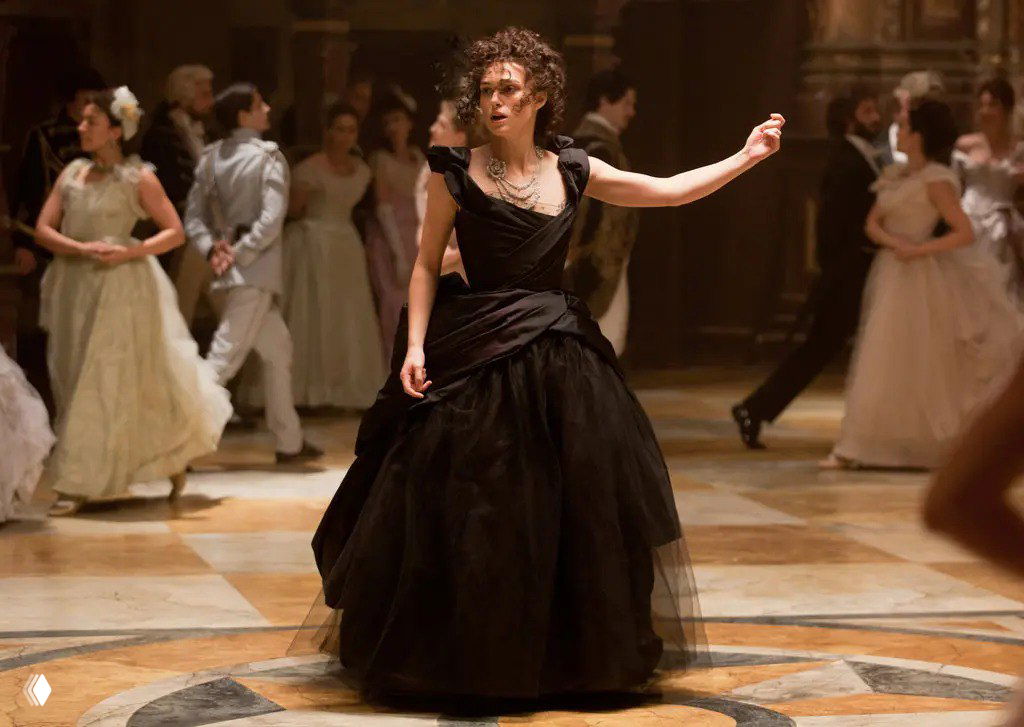 Героиня в пышном чёрном бальном платье на балу: кадр эпохальной сцены с гостями в пастельных нарядах, акцент на силуэте и текстуре ткани.