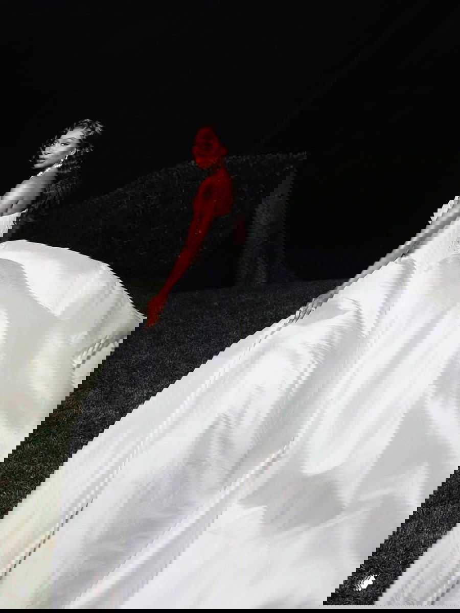 Винус в пышном свадебном платье с объёмной струящейся юбкой поворачивается в ночном саду — драматичный кадр с контрастом света и тьмы.