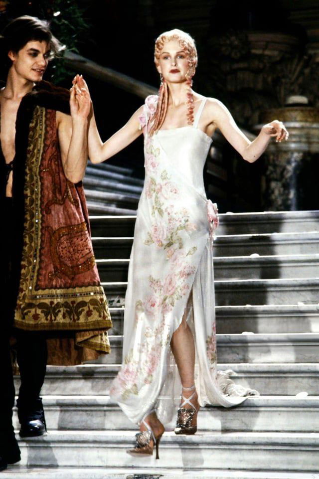 Лёгкое платье с цветочным принтом и тонкими бретелями, модель идёт по лестнице в романтическом образе из коллекции Dior 1998 — мягкие пастельные тона.