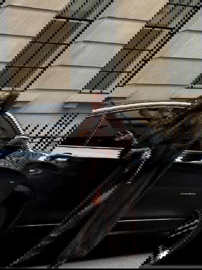 Высокая длинная тёмная шуба в пол на модели возле автомобиля, образ с высокими сапогами и аксессуарами, выглядит очень элегантно