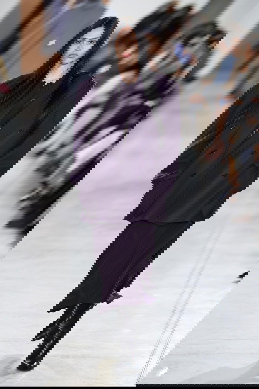 Показ: модель в глубоких тёмно-фиолетовых оверсайз жакете и платье на подиуме — минималистичный runway-образ с насыщенным оттенком.