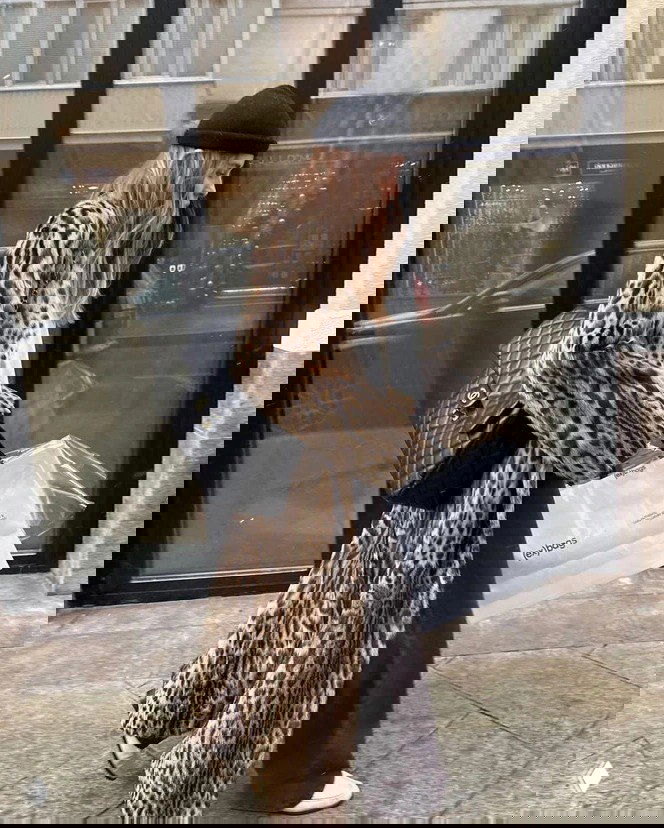 Длинное леопардовое пальто на прохожей в шапке, образ в анималистичном принте на фоне городского витрины и сумки Chanel