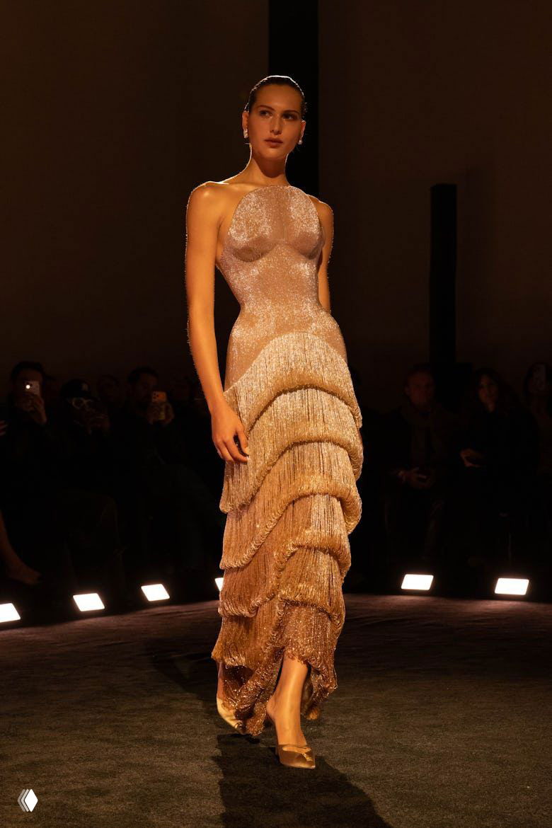 Длинное облегающее платье с каскадом бахромы и блеском, силуэт модели в центре круга подиума демонстрирует тонкую работу отделки Schiaparelli.