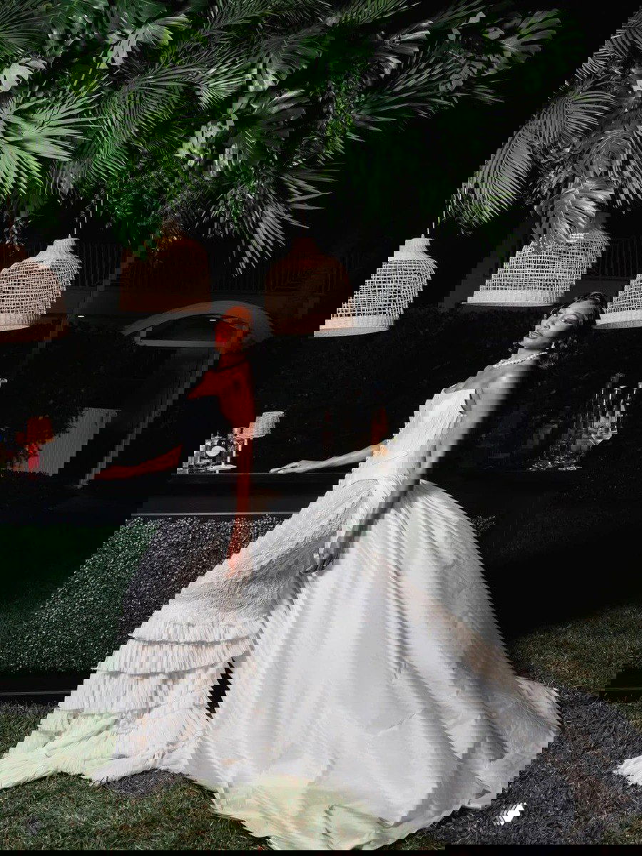 Винус у барной стойки в длинном белом платье с шлейфом; ночная атмосфера с пальмами и подвесными светильниками подчёркивает гламур вечеринки.