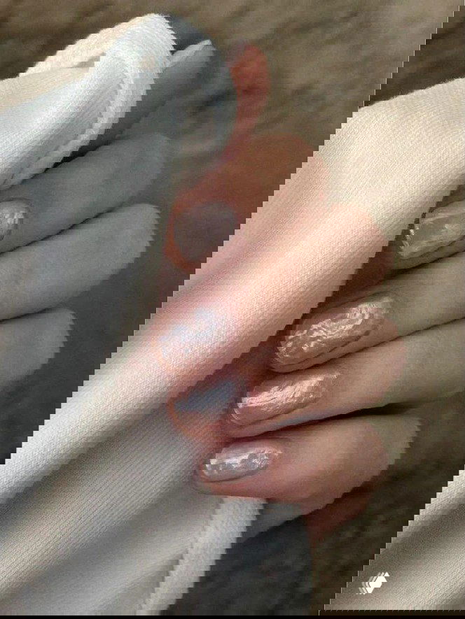 Крупный план коротких натуральных ногтей с полупрозрачным перламутровым покрытием на фоне белой ткани — нежный зимний маникюр.