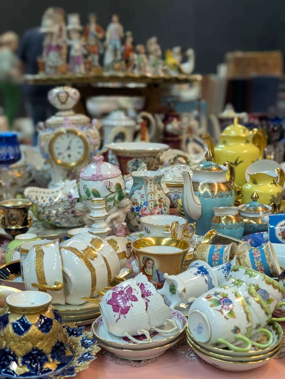 Стол с множеством винтажной посуды: фарфоровые чашки, чайники, блюдца и декоративные фигурки, разложенные на рынке в Москве.