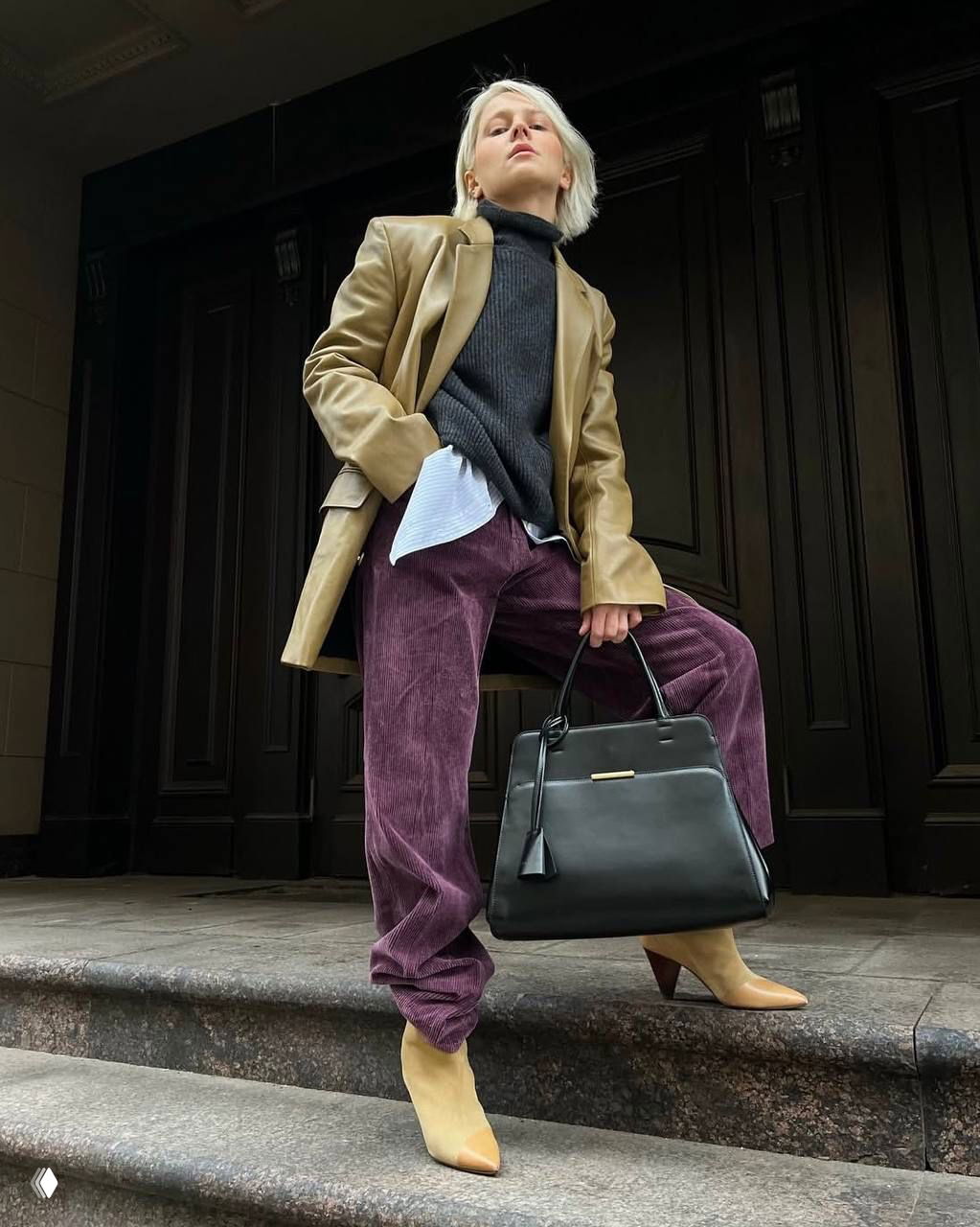 Повседневный образ с вельветовыми фиолетовыми брюками, бежевыми ботильонами и большой чёрной сумкой — текстуры и контрастные нейтралы рядом с фиолетовым.
