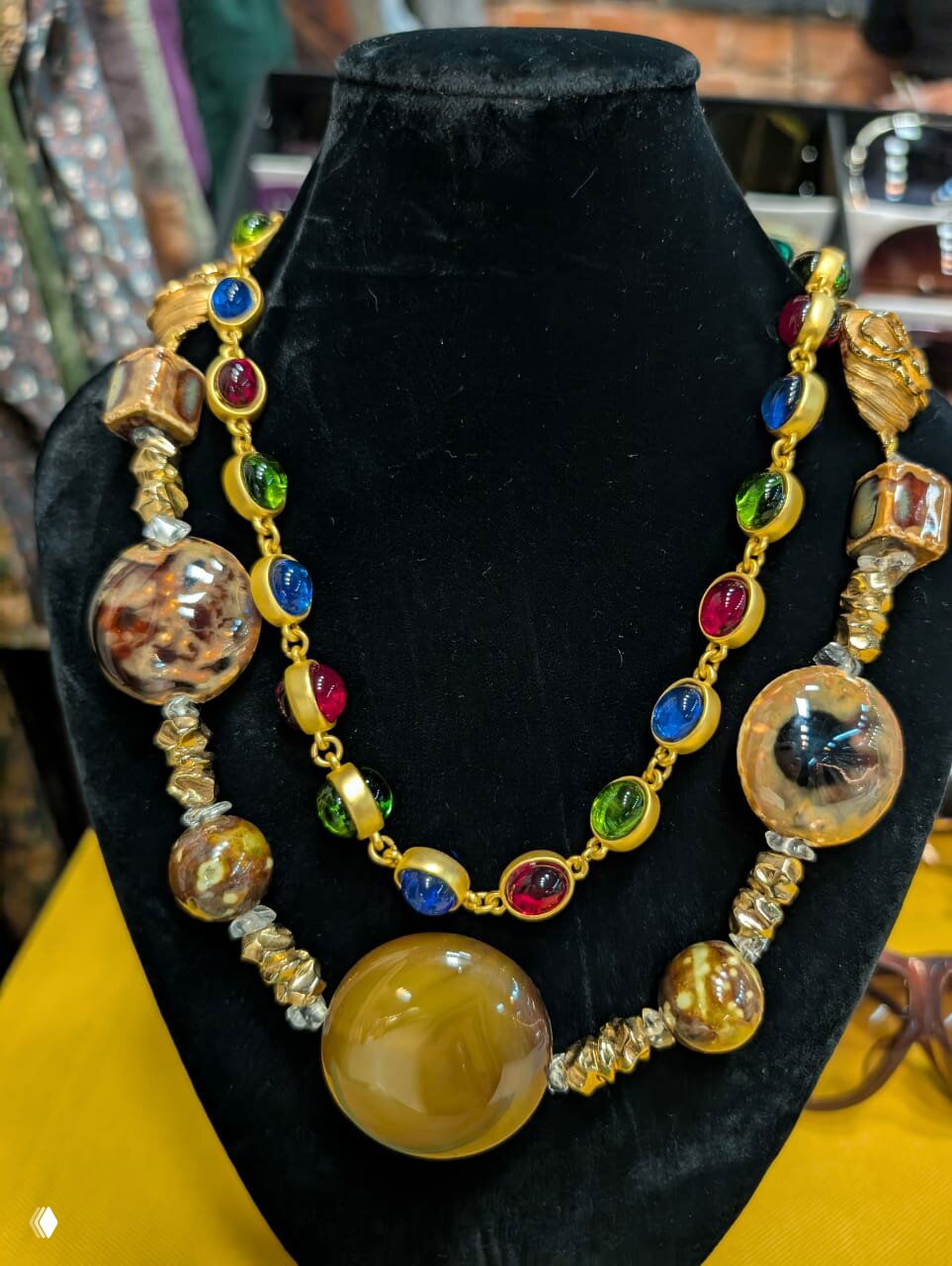 Витрина с винтажными украшениями: крупные бусы и ожерелья с разноцветными камнями на черном бархатном манекене в холле рынка.