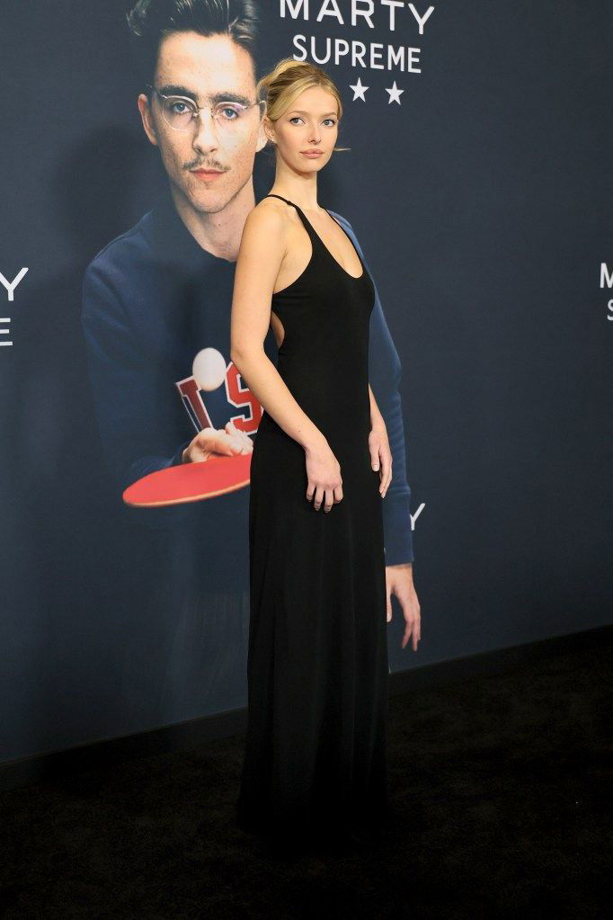 Вид сбоку на ту же женщину в чёрном платье Calvin Klein на красной дорожке, элегантная поза и аккуратная причёска в пучок