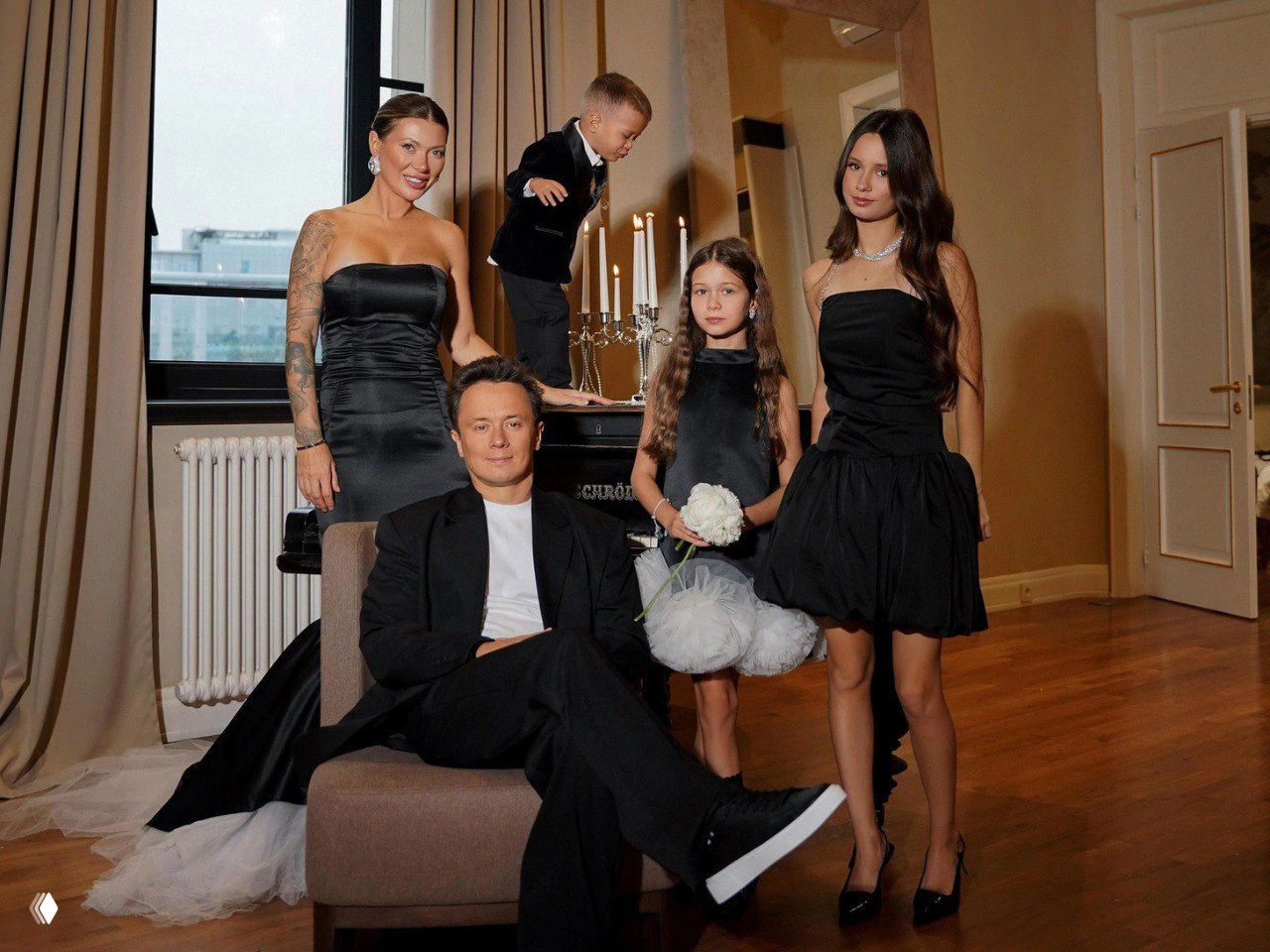 Семейный портрет в интерьере: взрослый мужчина в костюме сидит в кресле, рядом две девочки и женщина в вечерних нарядах, торжественная атмосфера.