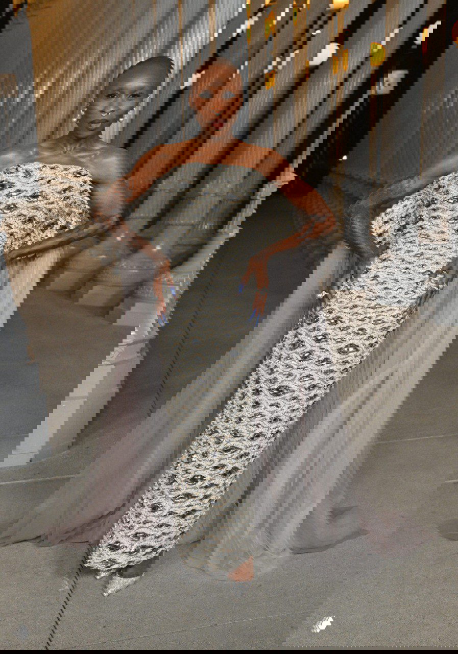 Полный рост женщины в фактурном серебристом платье с вышивкой и прозрачной накидкой на фоне инсталляции колонн LACMA, вечерний кадр.