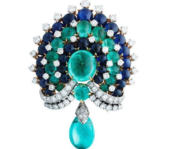 Крупный план винтажной броши с зелёными и синими драгоценными камнями и каплевидным подвесом; детализированный вид огранки и металла.
