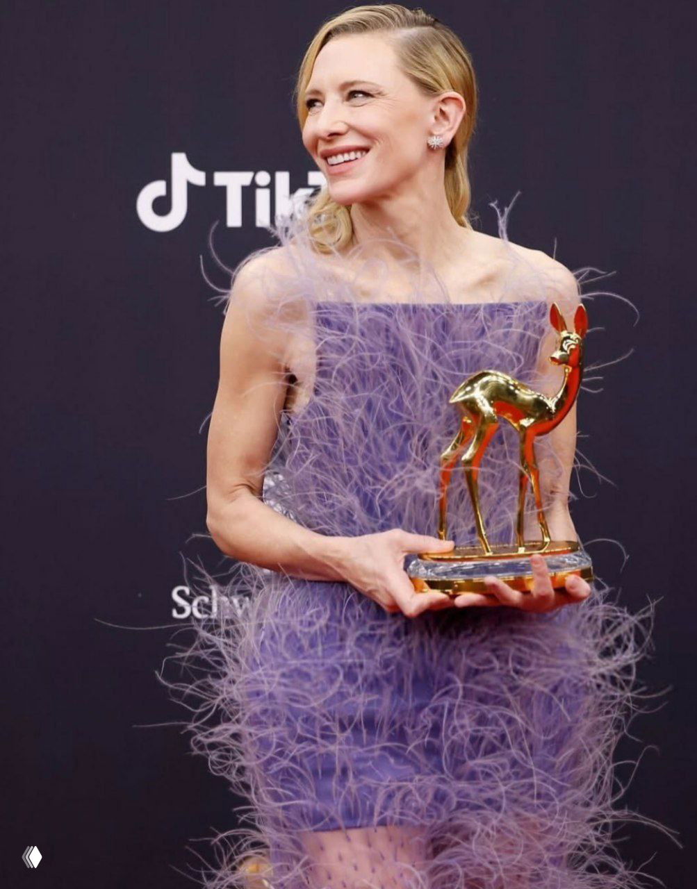 Кейт Бланшетт держит статуэтку Bambi в фиолетовом платье Stella McCartney, на платье видны имитации страусиных перьев из растений.