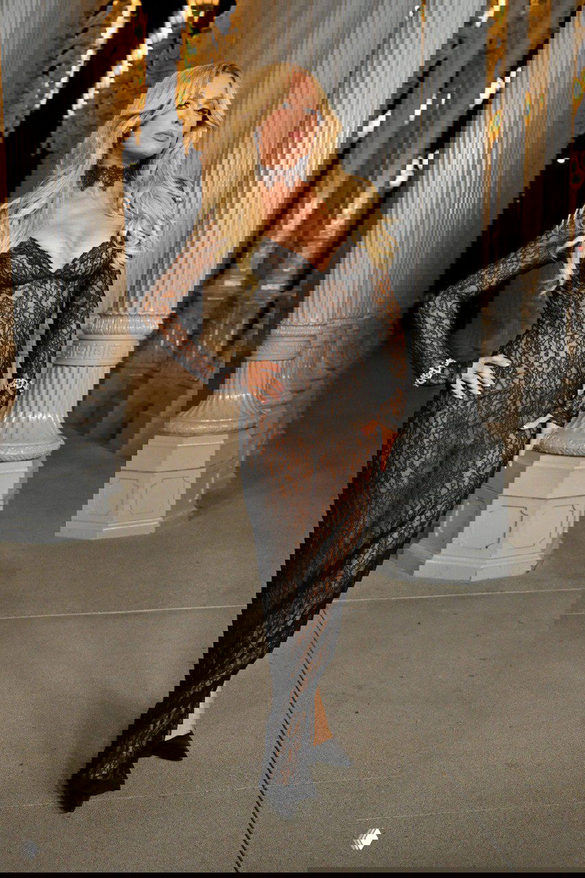 Женщина в черном кружевном платье в обтяжку позирует на дорожке с колоннами — прозрачный силуэт и готические аксессуары.