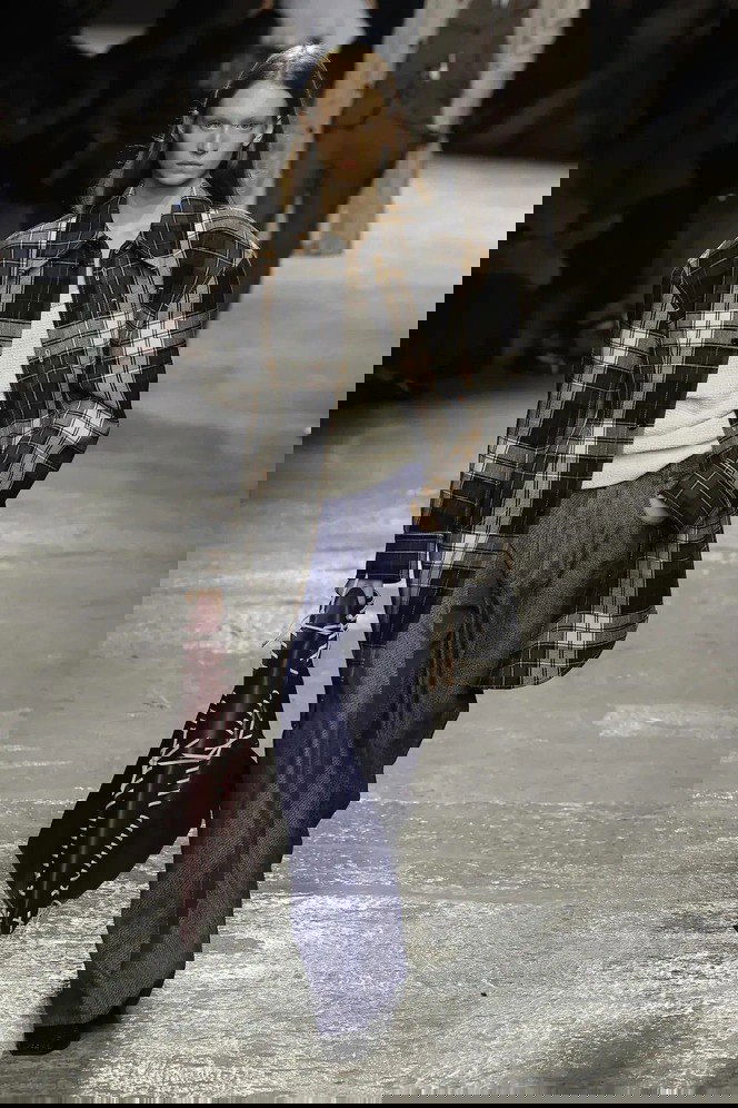 Модель на показе в крупной тёмно-коричневой и бело-серой клетчатой рубашке, светлый свитер и широкие брюки — демонстрация осеннего тренда в клетку.