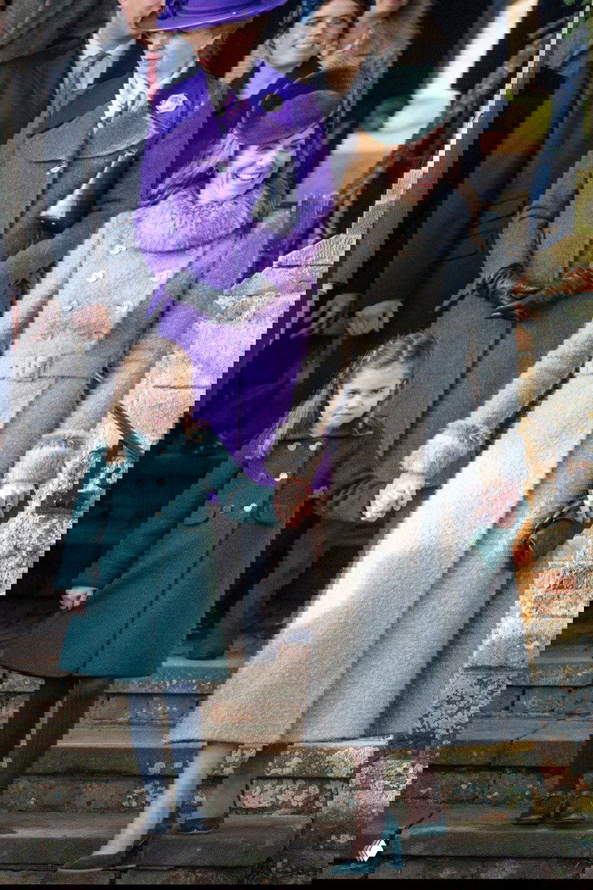 Женщина в светлом длинном пальто с меховой отделкой и ребёнок в зелёном пальто спускаются по ступеням на рождественском мероприятии в церкви.