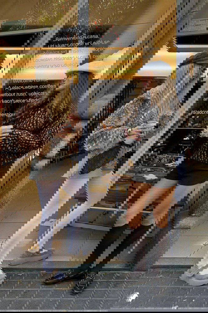 Две девушки у входа в кафе в пятнистых куртках — принт «Бэмби», береты и стаканы кофе; уличный городской кадр для вдохновения.