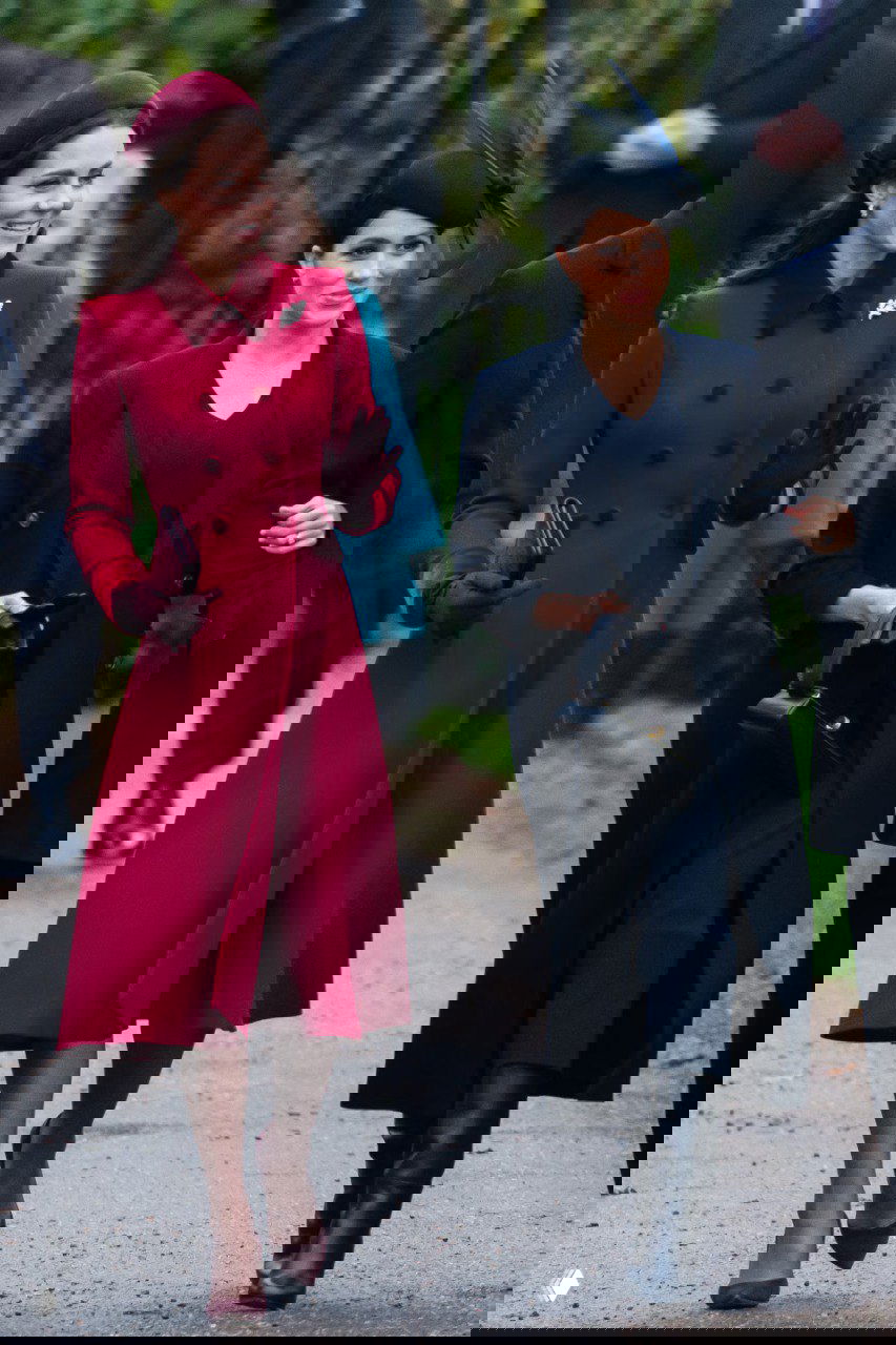 Две женщины идут рядом по дорожке: одна в тёмно-красном пальто, другая в тёмном плаще и шляпке, настроение праздничного парада заметно в кадре.