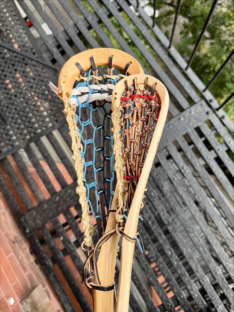Крупный план двух деревянных клюшек для лакросса с плетёными сетками, сложенных на металлической пожарной лестнице на улице.