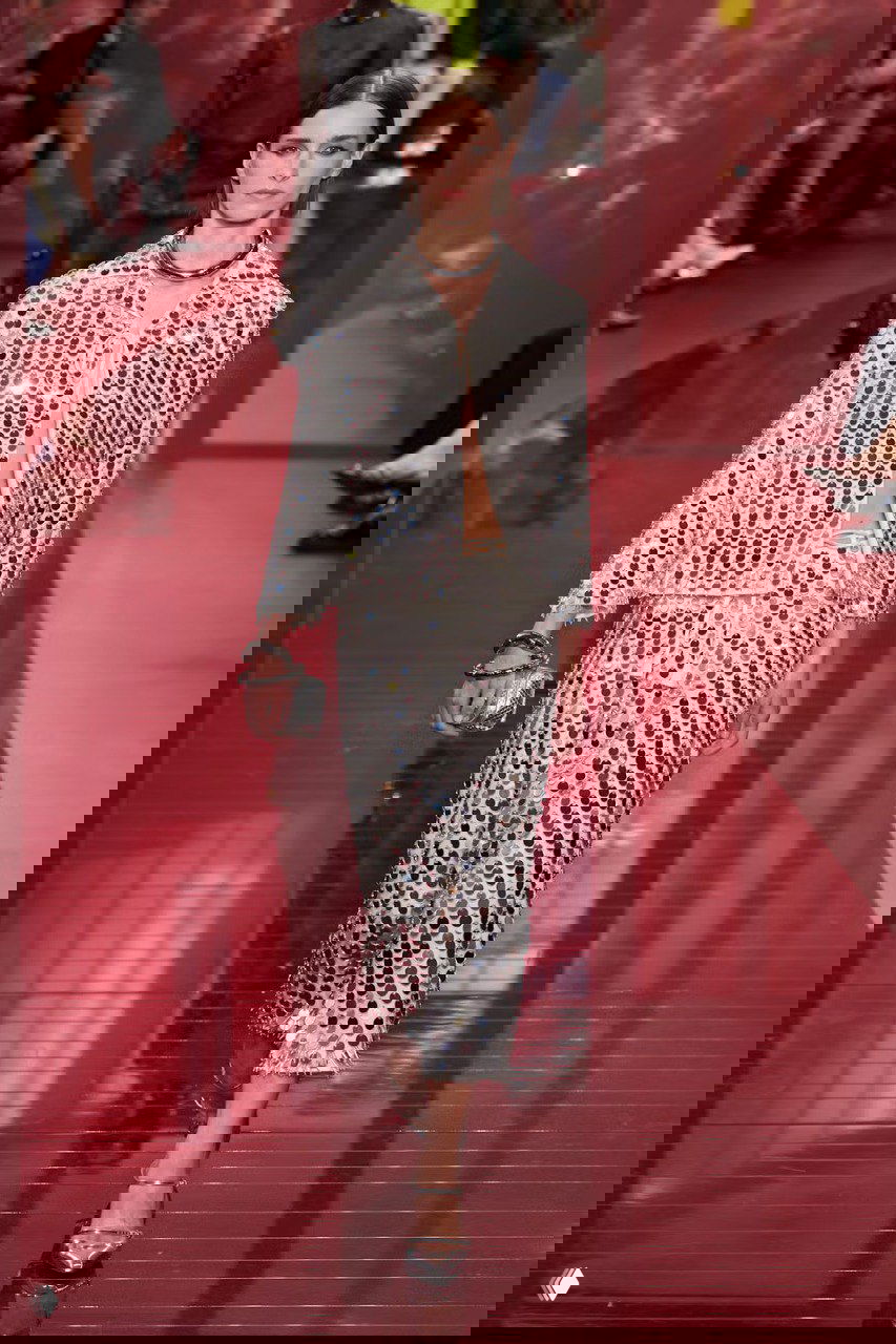 Модель на подиуме в серебристом наряде с крупными пайетками и зеркальными деталями, подчёркивающими праздничный блеск и фактуру ткани.