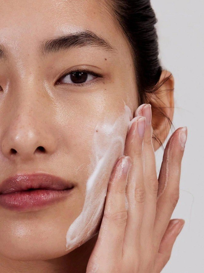 Крупный план лица девушки с пенящимся средством на щеке; иллюстрация способа нанесения и состояния увлажнённой, чистой кожи.