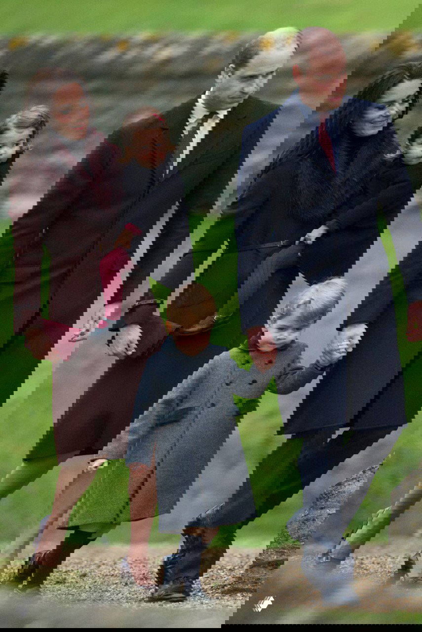 Семейный кадр: двое взрослых и двое детей в тёплой одежде идут по газону — классические пальто и детские пальто создают праздничную картину.