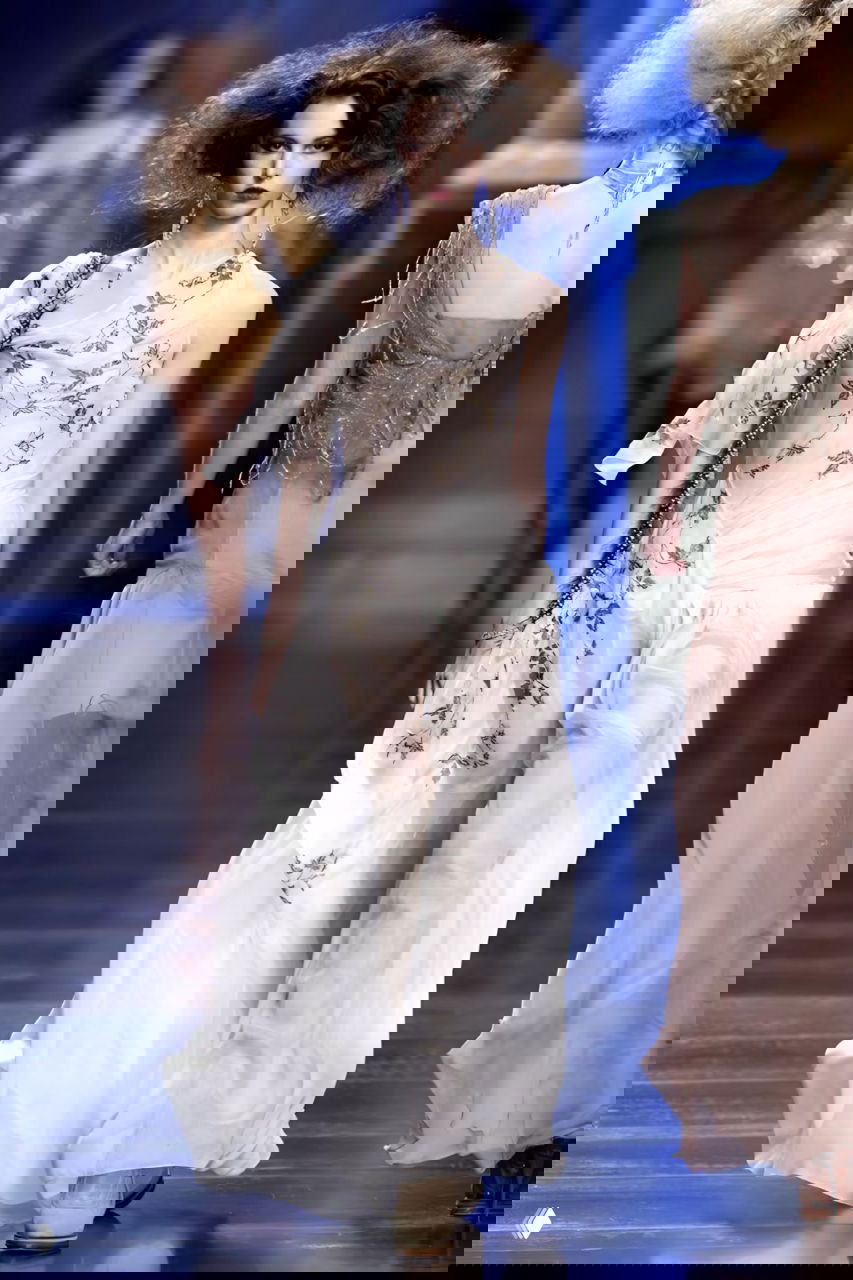 Модель в полупрозрачном платье с вышивкой и длинными серьгами на показе Dior AW 2010 — лёгкость тканей и тонкая отделка заметны в деталях.