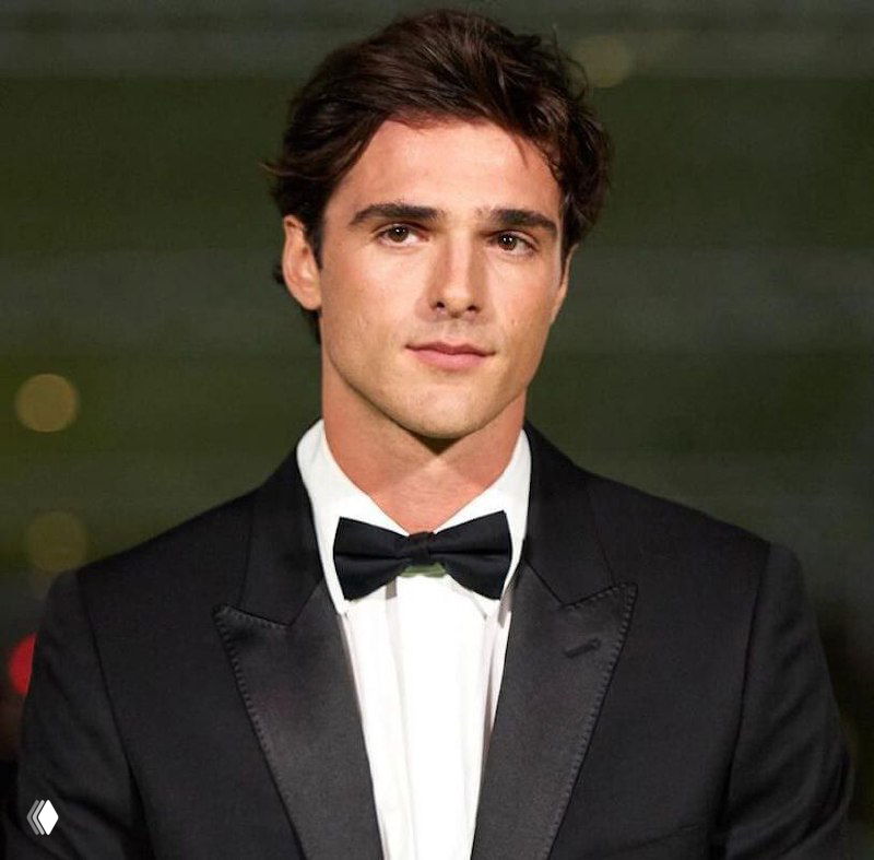 Портрет другого молодого мужчины в смокинге и бабочке, серьёзный и сосредоточенный взгляд, студийное или красно‑ковровое окружение.