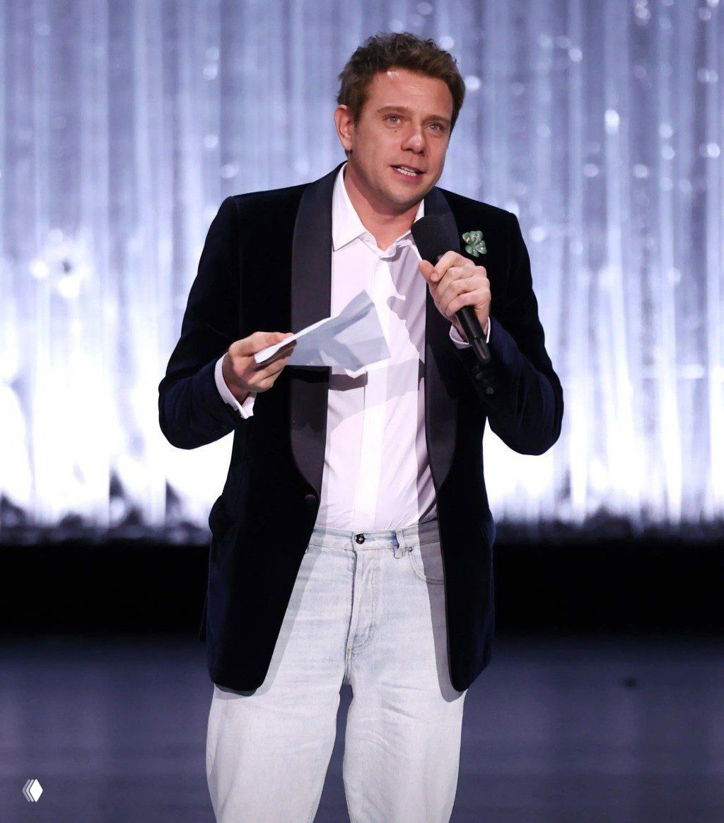 Джонатан Андерсон на сцене церемонии Fashion Awards 2025 в Альберт‑холле: в смокинге, с микрофоном и листом бумаги, обращается к публике