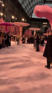Панорамный вид на подиум Chanel с высокими розовыми и бежевыми грибами, публика под стеклянным куполом Галереи наблюдает за шоу