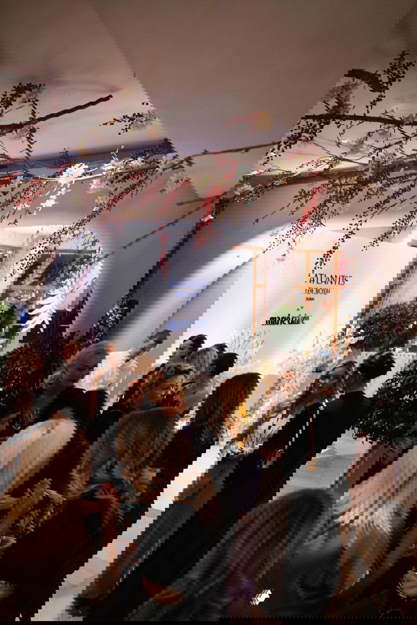 Гости и гостьи на гала-ужине Atlantis The Royal x Marie Claire в ресторане Onest в Москве, люди общаются на фоне цветочной декорации и брендированной стены.