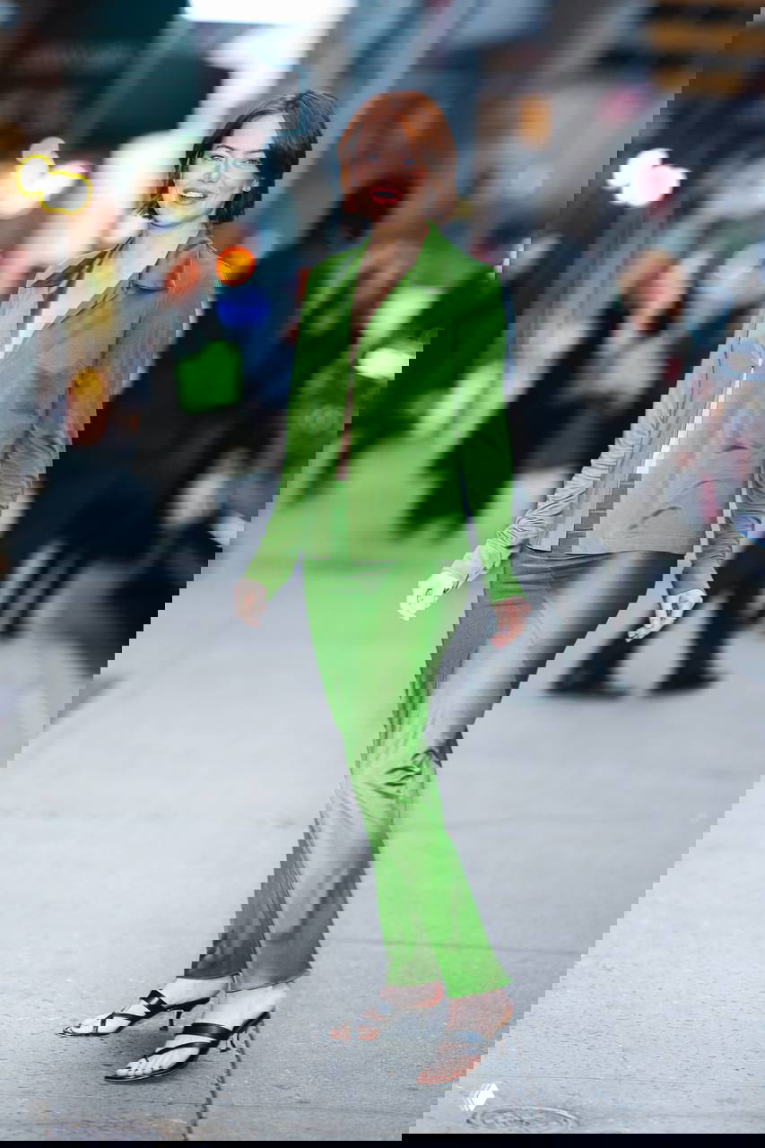 Актриса в ярко‑зелёном двоечном ансамбле позирует на фоне городских огней и припаркованных автомобилей, улыбается камерaм.