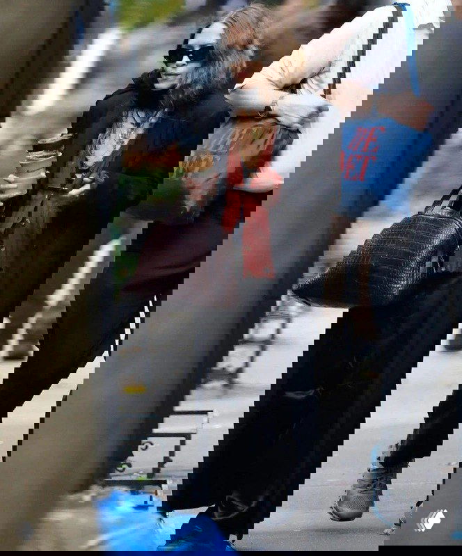 Женщина в длинном тёмном пальто на улице, волосы частично заправлены в воротник и верхнюю одежду, городской фон прогулки