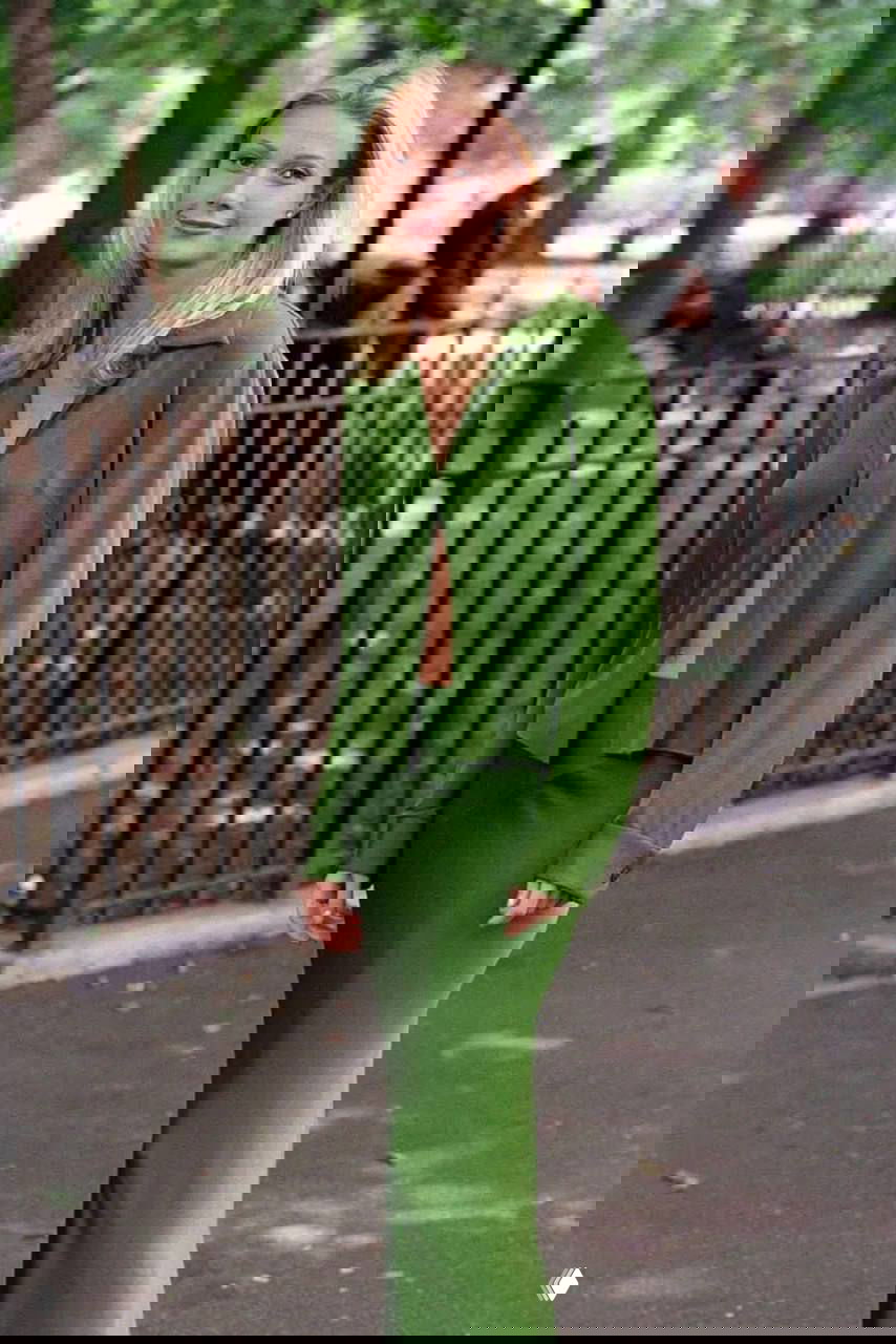 Ракурс в полный рост: актриса в зелёной длинной юбке и лёгкой рубашке идёт по городскому тротуару в открытой позе перед камерами.