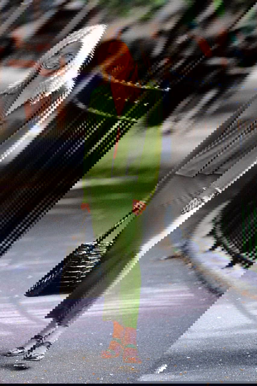 Архивный кадр: светловолосая актриса в зелёном платье и рубашке в парке — справочный снимок культового образа 1998 года на фоне деревьев и ограды.