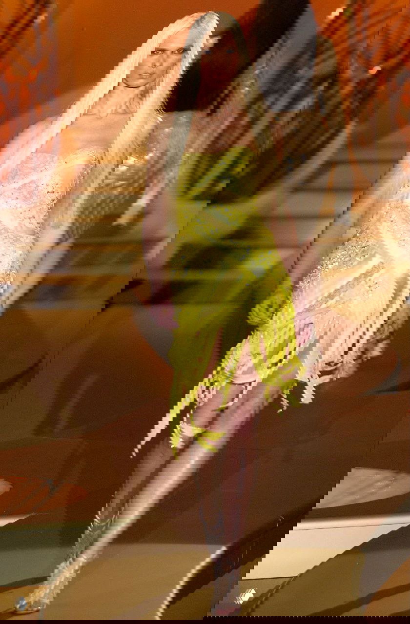 Модель в ярко-жёлтом мини-платье с бахромой и блёстками, динамичный образ кутюрной коллекции Versace 2004 на фоне золотого сценического оформления.