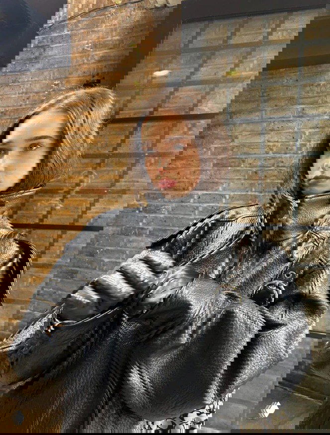 Модель в большом чёрном кожаном пальто с высоким воротником, пряди волос заправлены внутрь, акцент на фактуре верхней одежды