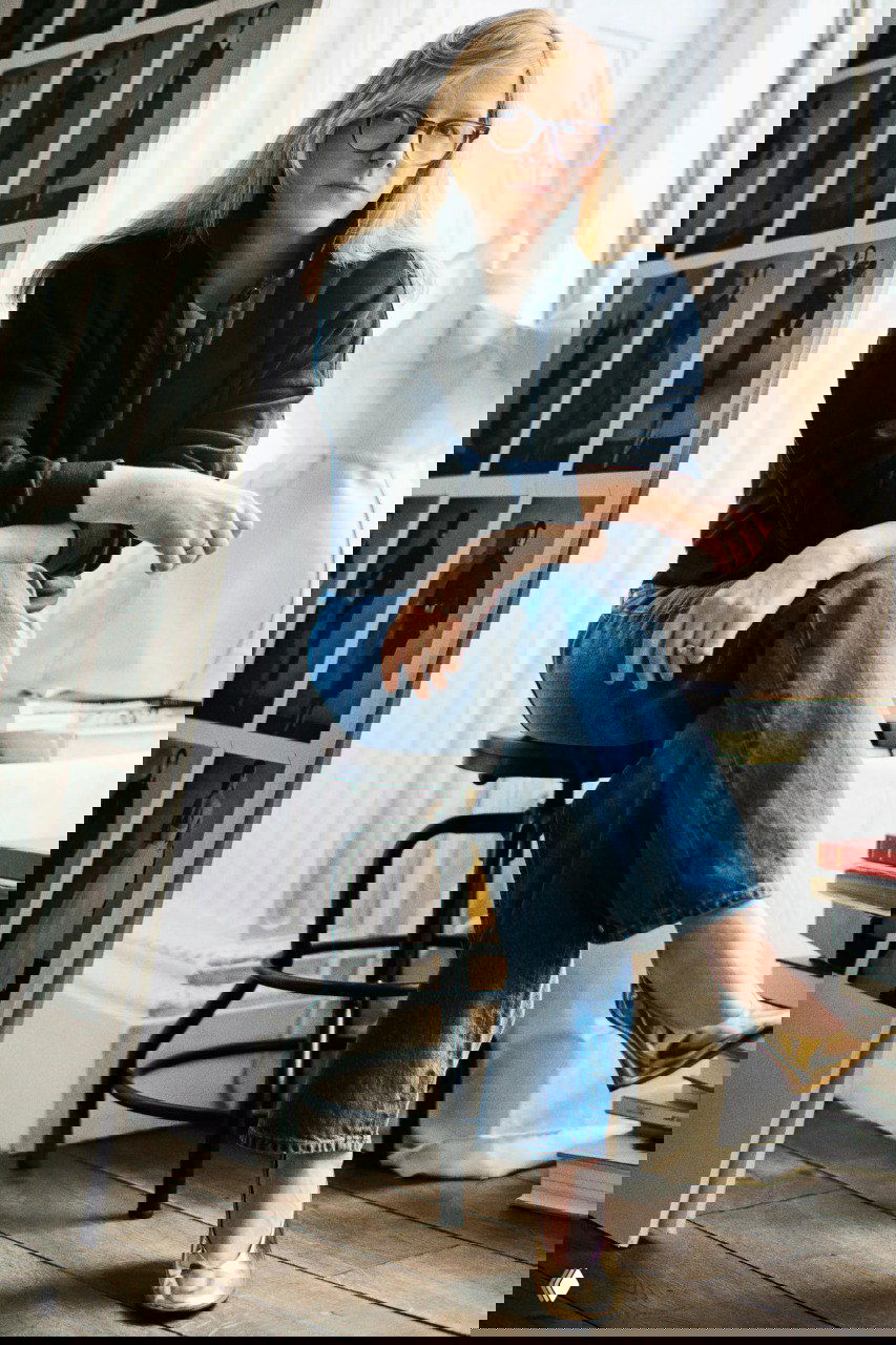 Портрет Сары Бёртон в студии: сидит в джинсах и золотых туфлях рядом с манекеном и фотоколлажем, видны тестовые ч/б съёмки.