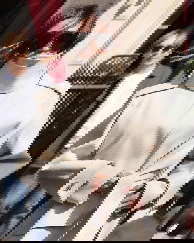 Женщина в светлом тренче с высоким воротником, волосы частично убраны внутрь воротника, крупные солнцезащитные очки и аксессуары