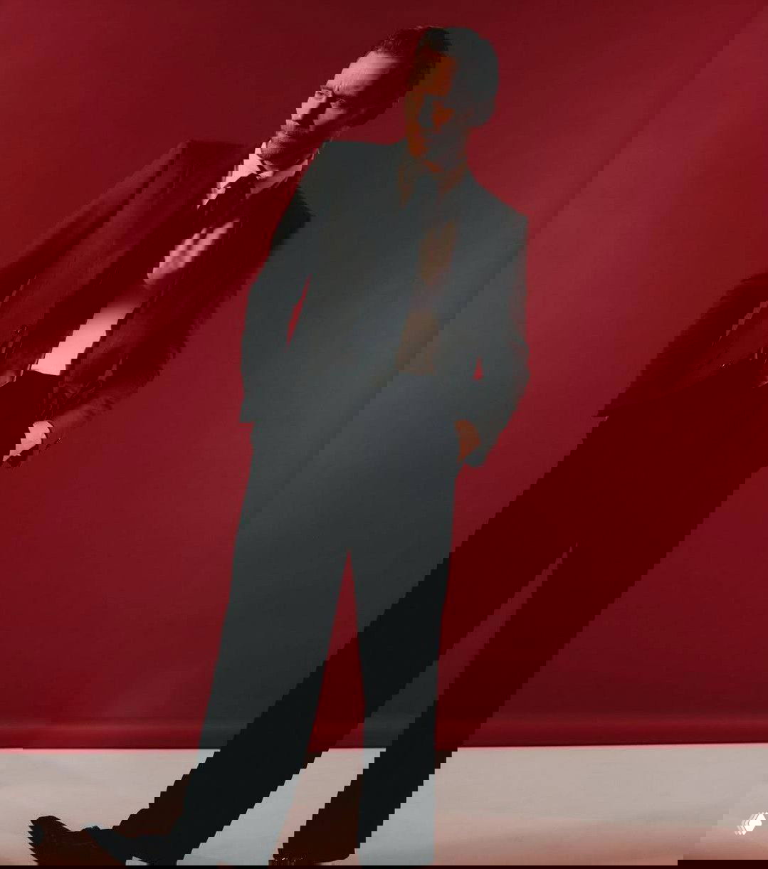 Полнофигурный студийный кадр мужчины в классическом костюме на красном фоне — стильная постановочная съёмка модного формата.