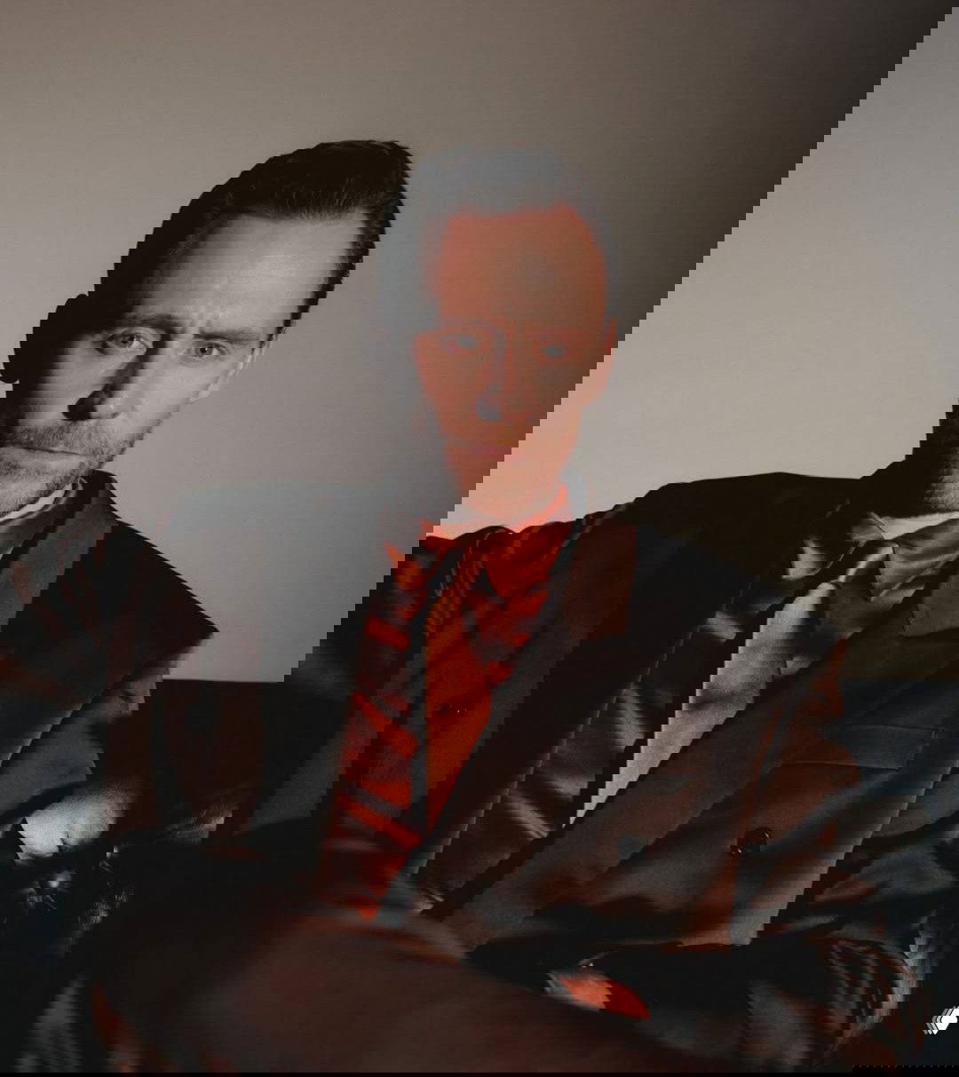 Мужчина в тёмном пиджаке и шёлковой рубашке в интерьерном кадре — расслабленная поза и мягкое направленное освещение для журнального разворота.