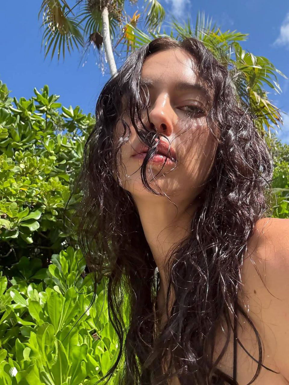 Крупный план Ирины Шейк на фоне тропической зелени и пальм, влажные распущенные волосы и солнечный свет — отпускная атмосфера и релакс.