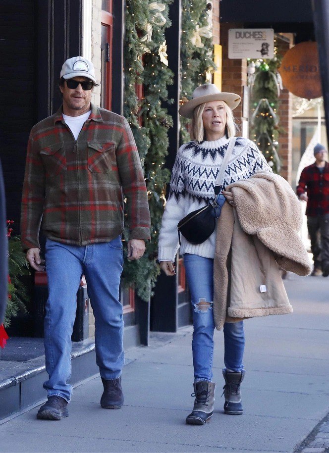 Пара идёт по улице в Аспене: женщина в скандинавском свитере и шляпе держит тёплую шубу, мужчина в клетчатой рубашке рядом.