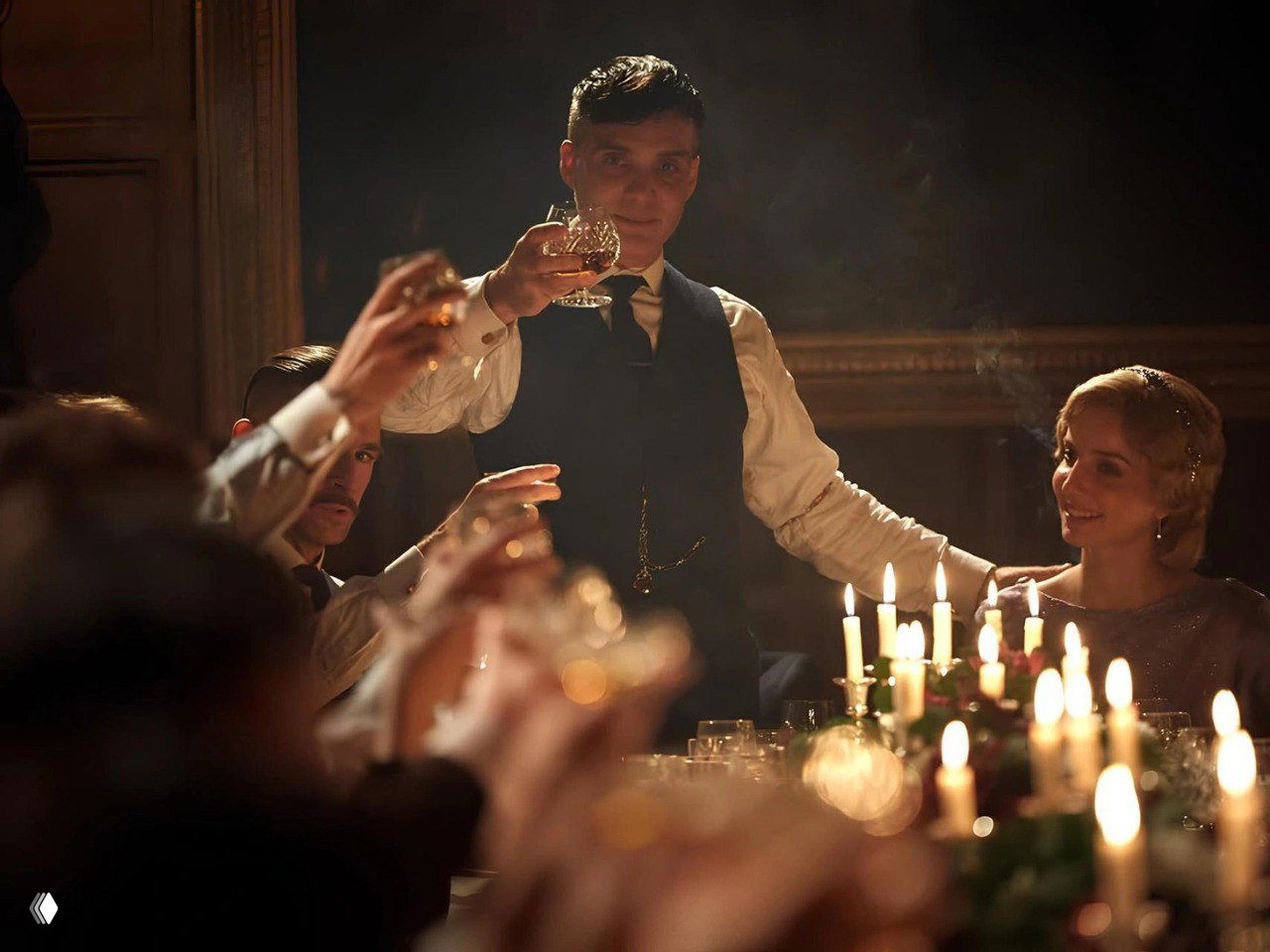 Килиан Мёрфи как Томас Шелби поднимает бокал за столом с гостями и свечами — кадр с тёплой подсветкой и дымкой.